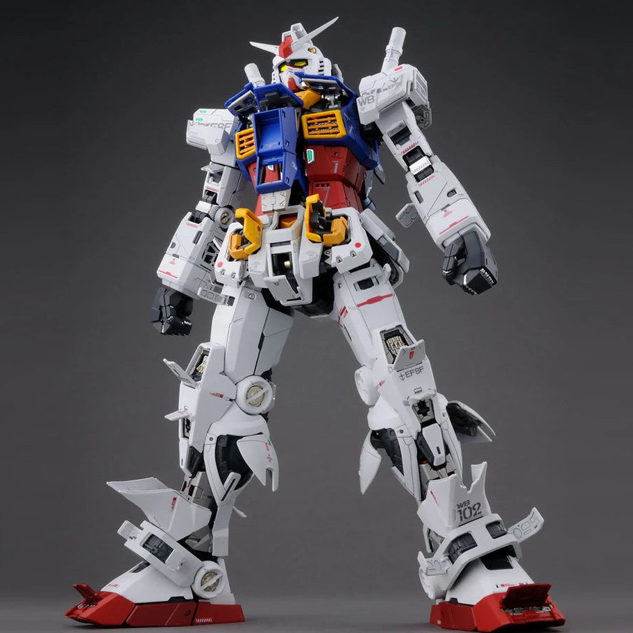 A highly detailed plastic model of a Gundam robot, shown in a dynamic standing pose against a dark gray studio background. The model is primarily white with prominent blue, red, and yellow armor panels, and red feet.